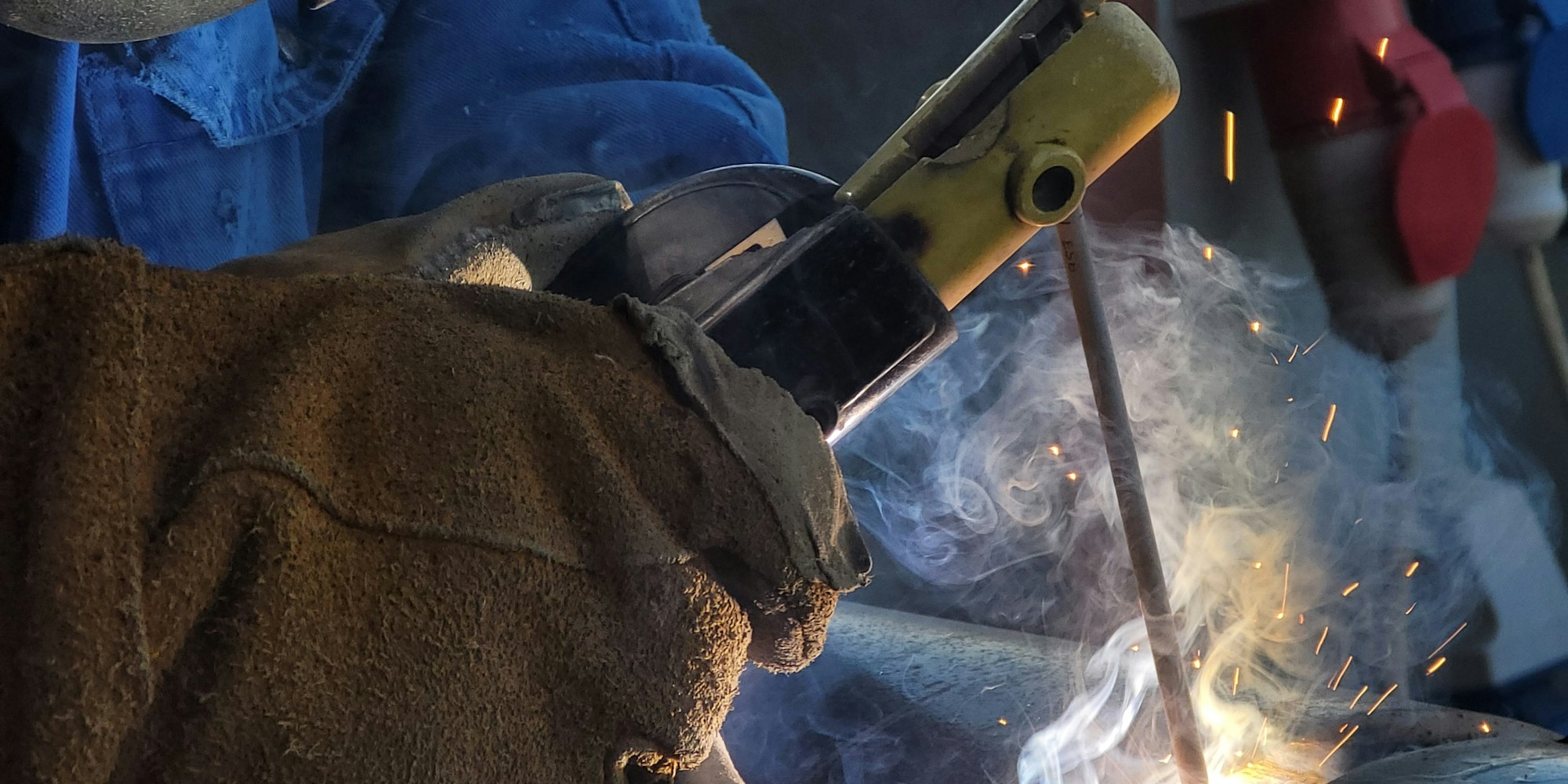 Worker in heavy-duty leather gloves at a manufacturing workstation